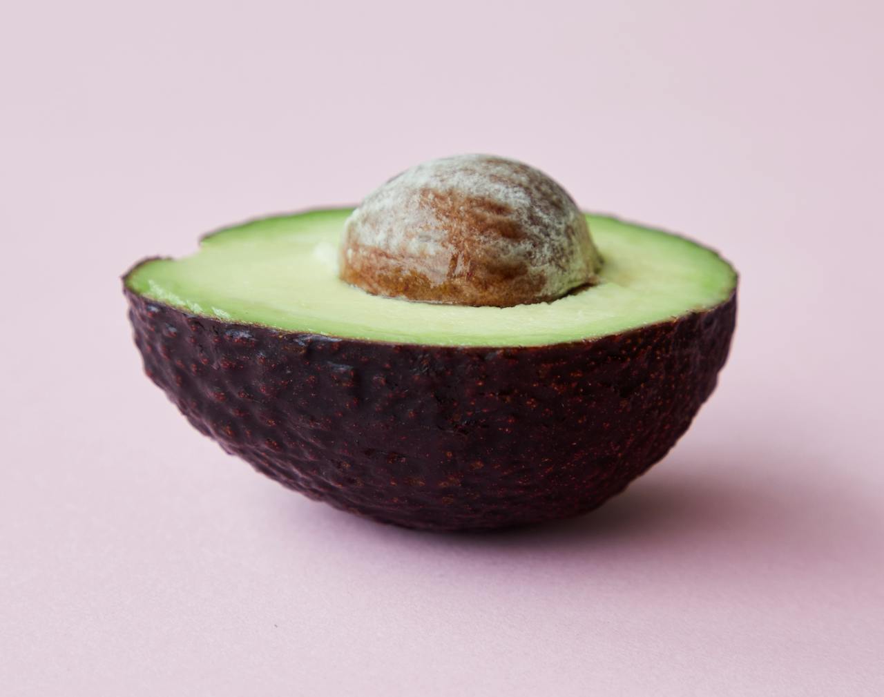 about-bg A ripe avocado half with seed on a pastel pink backdrop, showcasing its fresh and nutritious qualities.